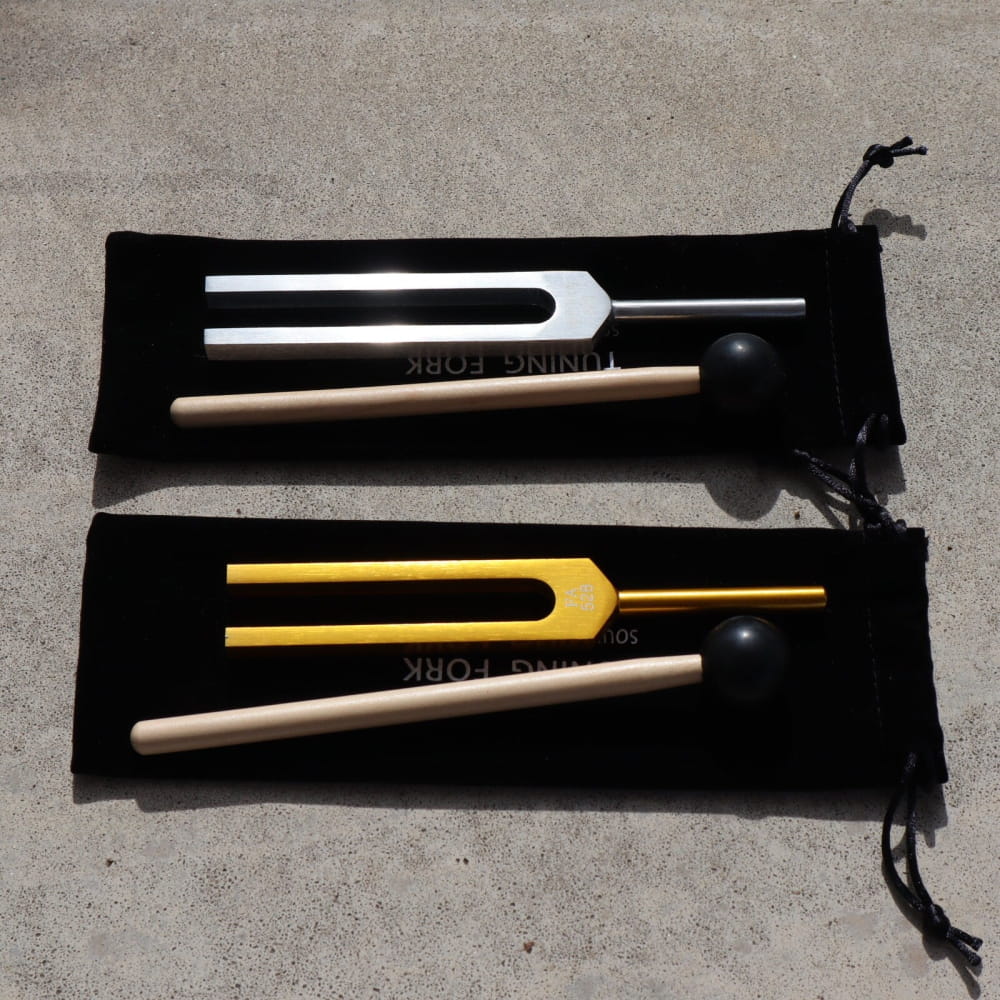 Two tuning forks with wooden strikers in drawstring pouches for vibration therapy