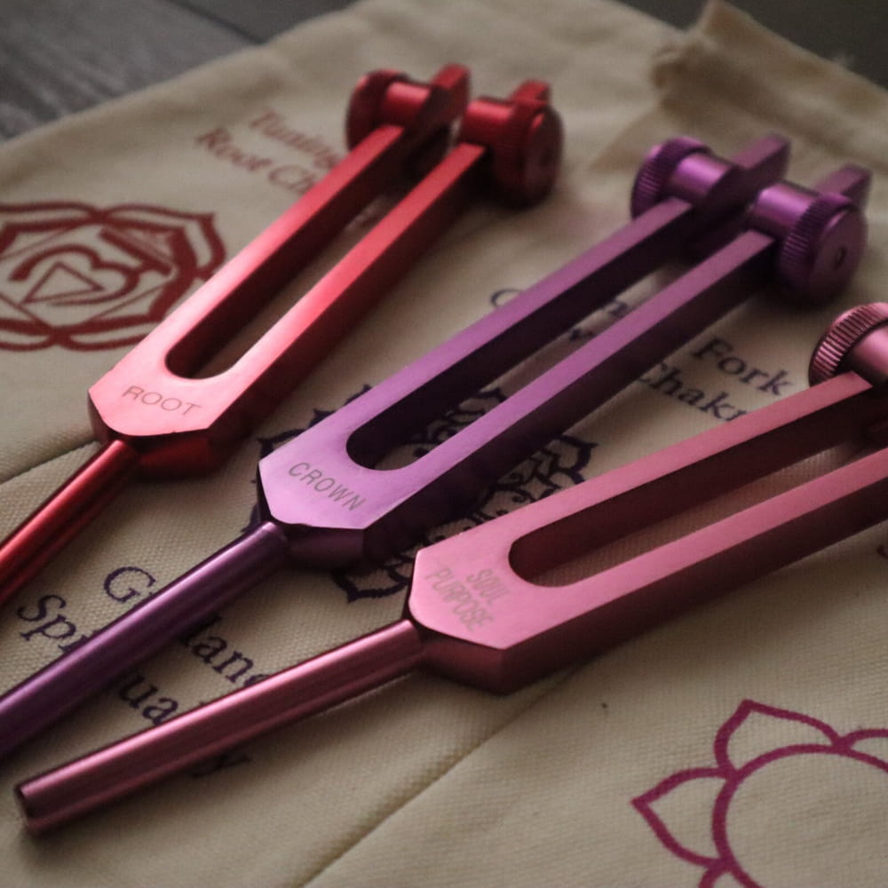 Three colorful tuning forks in red, purple, and pink metallic finishes for chakra healing