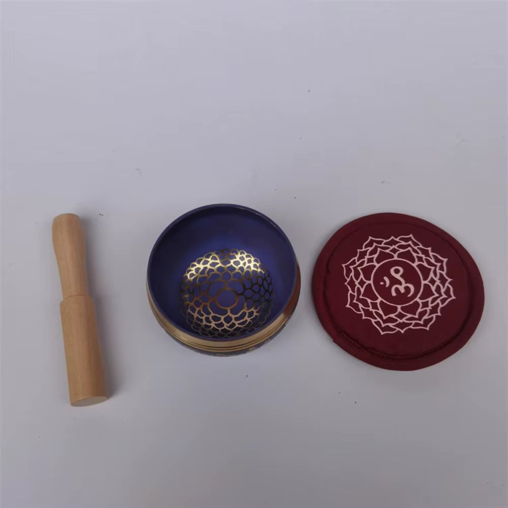 Two embroidered meditation cushions with a wooden rolling pin beside a colorful brass Tibetan Singing Bowl