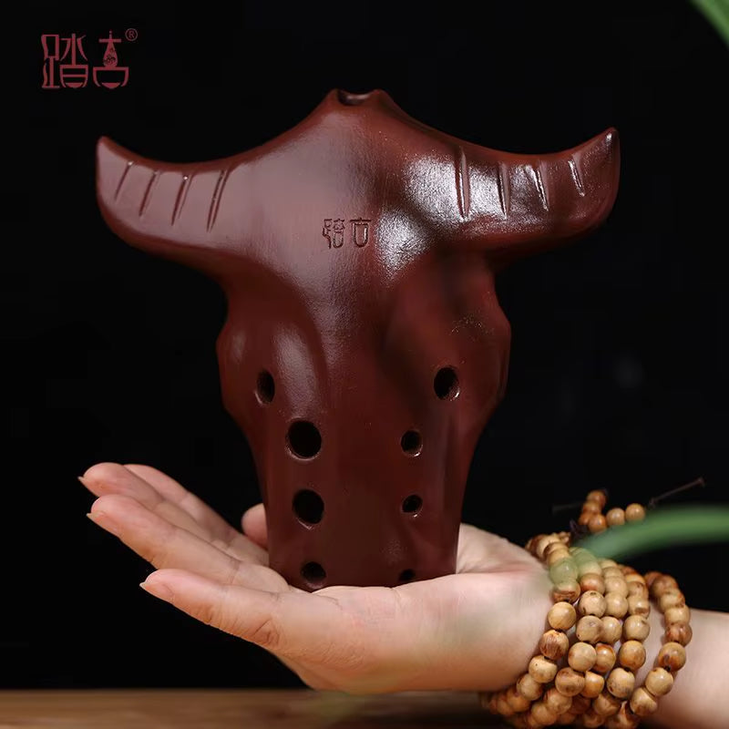 Brown clay ocarina shaped like a bull’s head with 10 finger holes for music playing