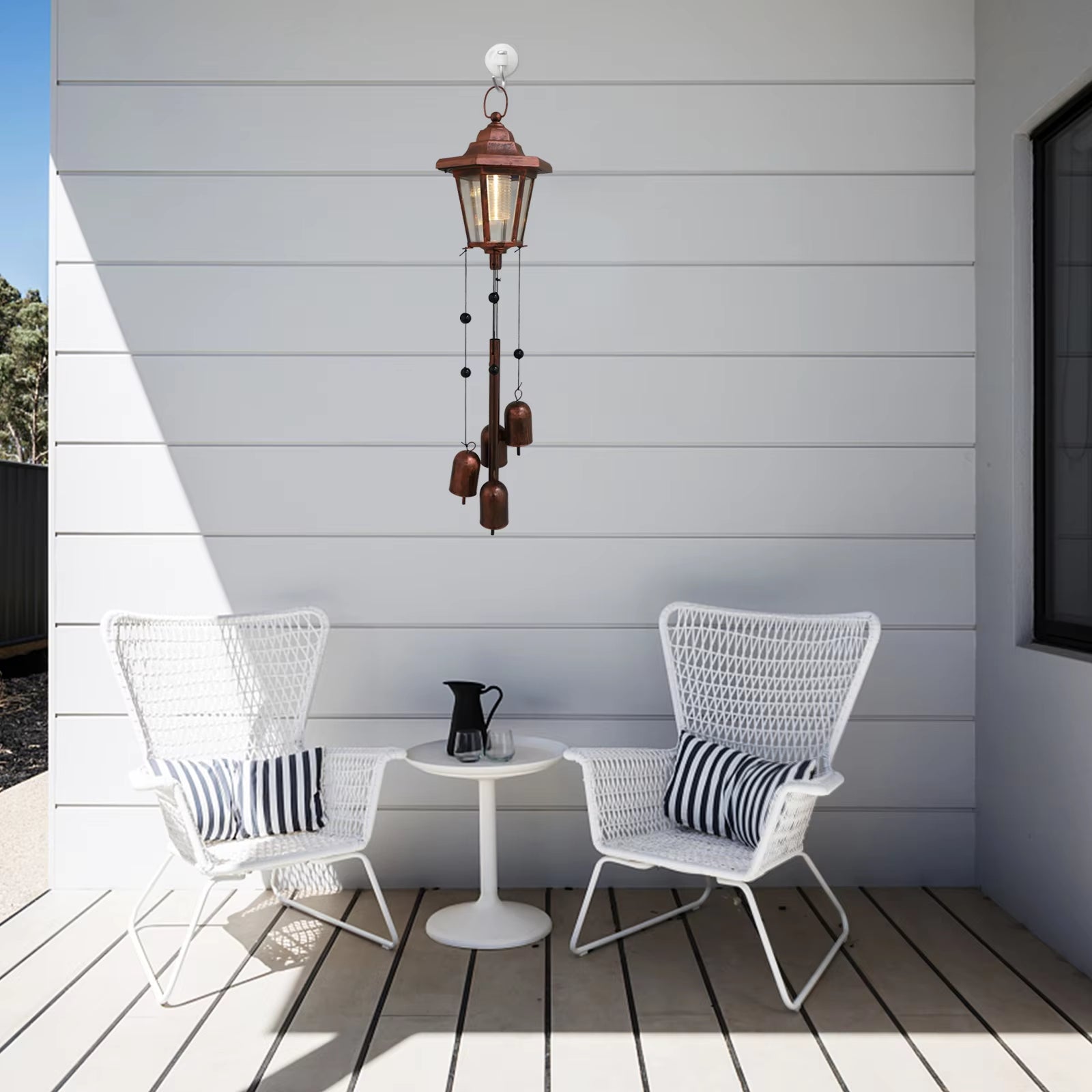 Two white wicker chairs with striped pillows and a round white table in a garden setting