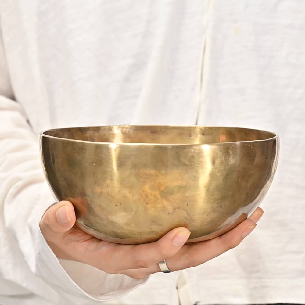 Golden Tibetan singing bowl held in hands with white sleeves for meditation healing