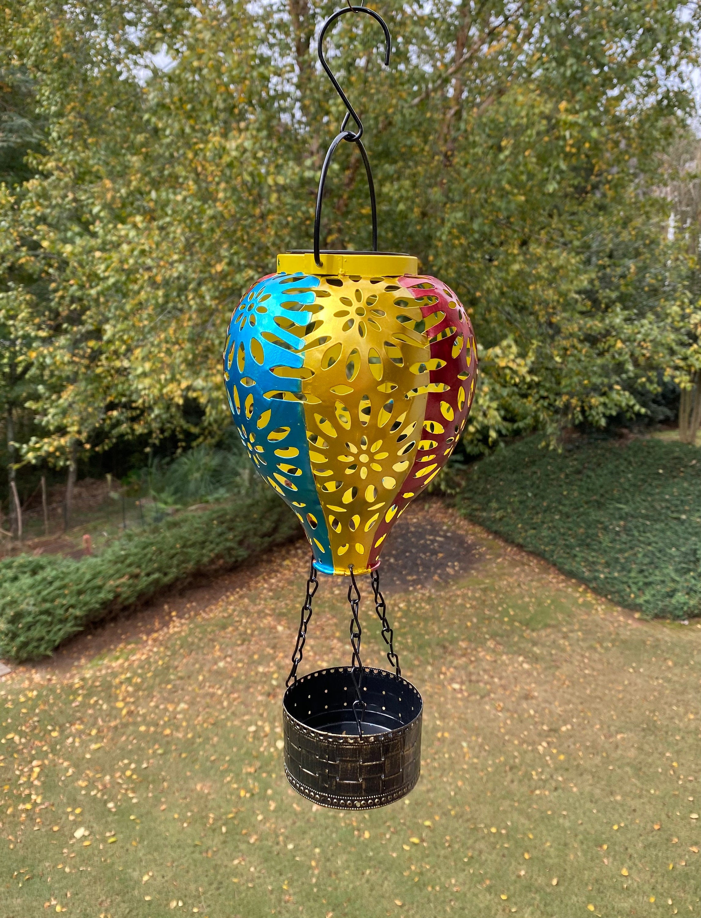 Colorful metal lantern with cutout patterns hanging from a hook for outdoor decor