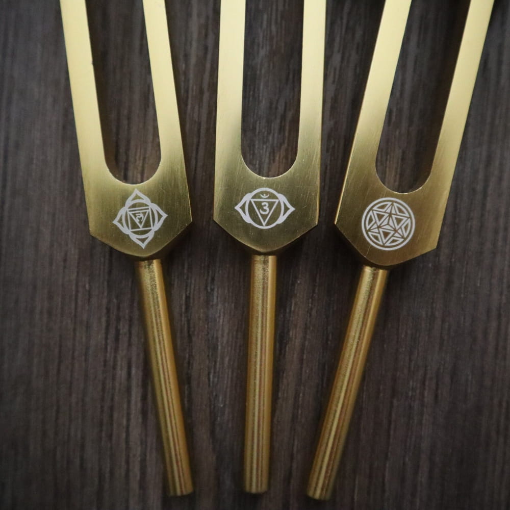 Three brass tuning forks with mystical symbols from a 24K Gold Chakra Tuning Fork Set