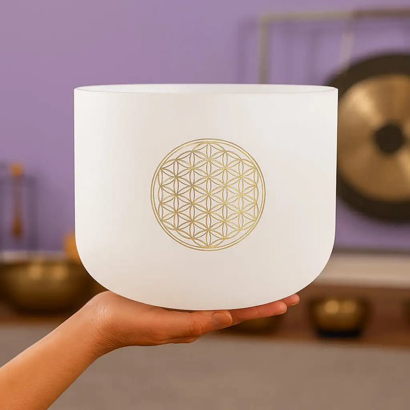 A white frosted glass crystal singing bowl with a gold-colored flower of life design etched on its side.