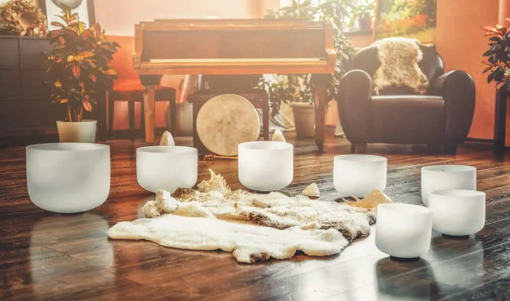 Set of seven frosted glass singing bowls arranged on a wooden floor with a sheepskin rug beneath them.