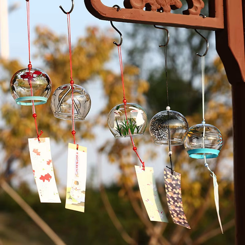 Glass wind chimes with decorative paper tags hanging from ornate hooks for outdoor decor