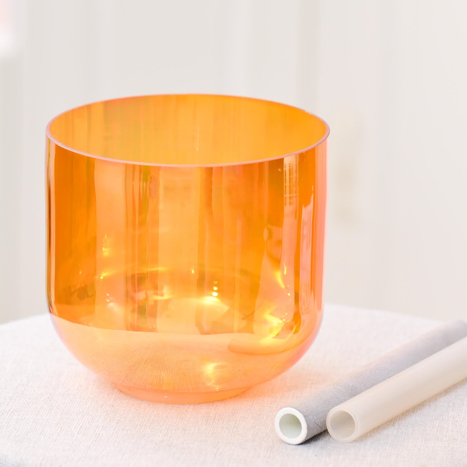 Orange translucent crystal singing bowl with white mallets for chakra meditation