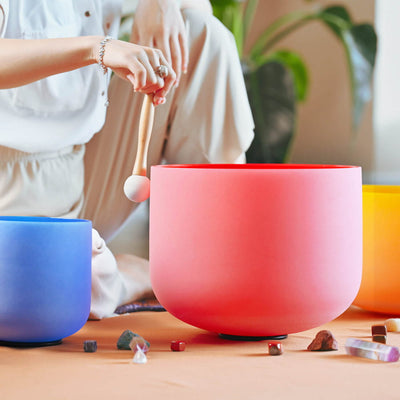 Pink crystal singing bowl with blue and orange bowls and scattered crystals