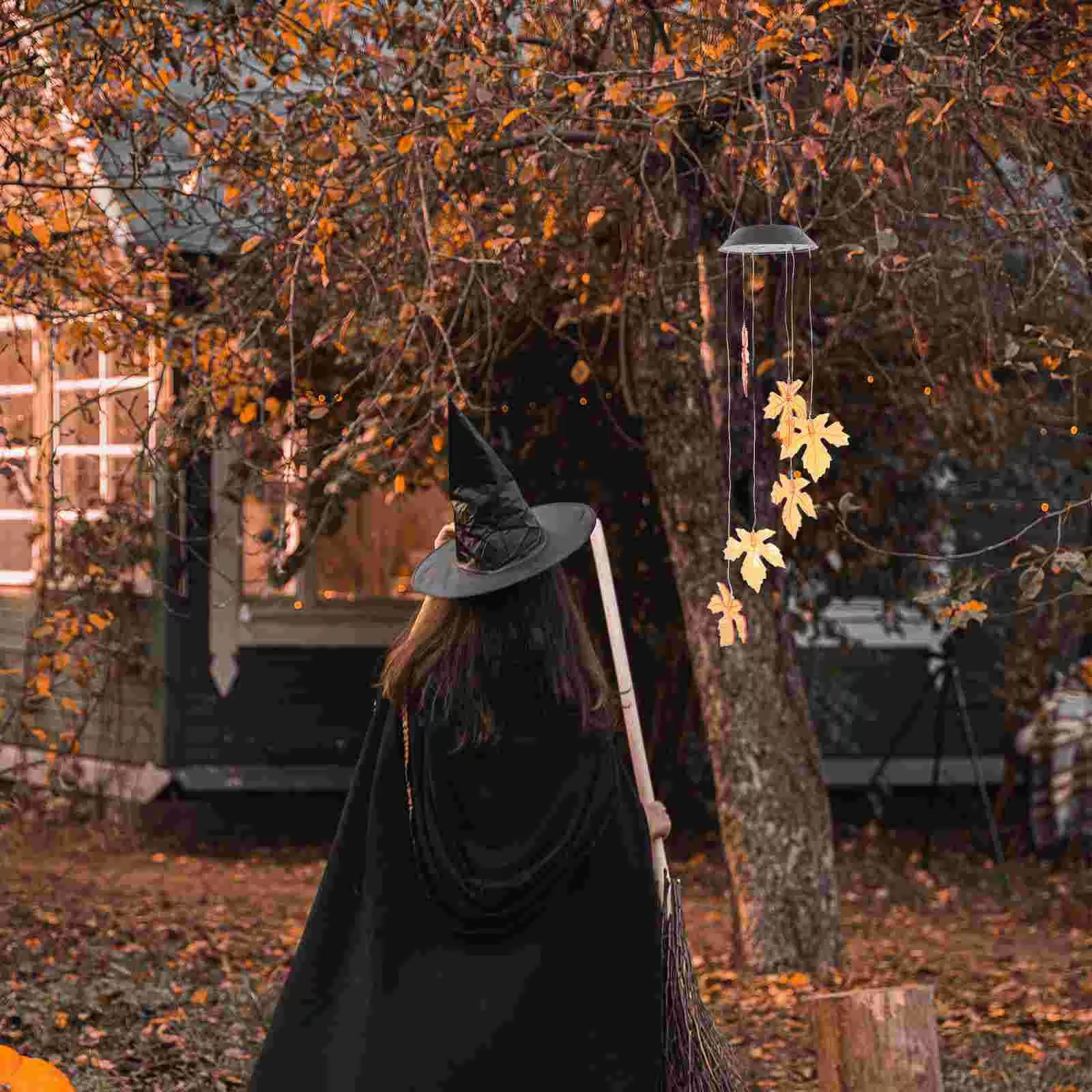 Witch in black cloak and hat beside Solar Wind Chimes Halloween Pumpkin Light Decor