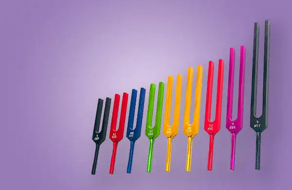 A set of colorful tuning forks arranged in ascending order, each with a distinct hue and engraved markings on the handle.